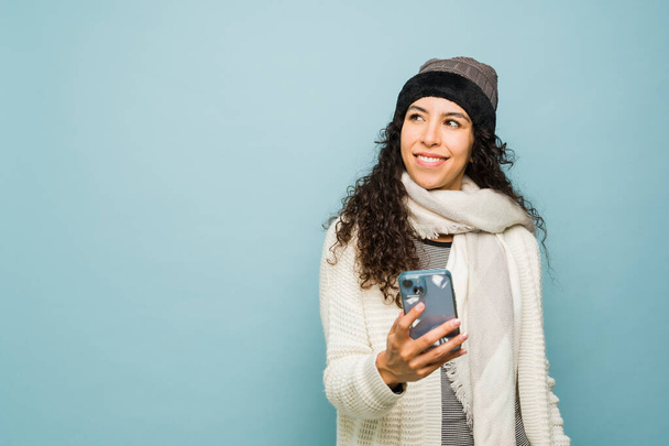 Удумлива іспаномовна жінка думає про зимовий сезон під час друку або використання соціальних медіа на смартфоні відчуває холод - Фото, зображення