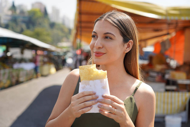 Zbliżenie pięknej dziewczyny jedzącej tradycyjne brazylijskie jedzenie Pastel de Feira w Sao Paulo, Brazylia - Zdjęcie, obraz