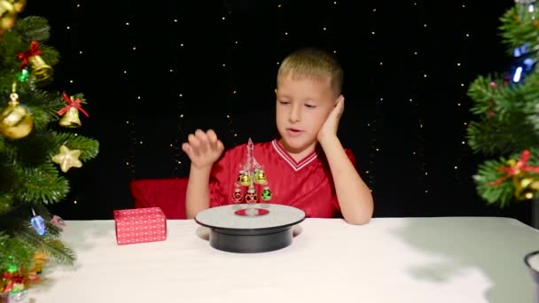 Aranyos fiú ül egy kis díszített karácsonyfa mellett - Felvétel, videó