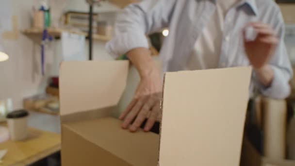 Oříznutý záběr ženy těsnění lepenkové krabice s průhlednou lepicí páskou při přípravě balíčku pro zásilku objednávky v doručovací služby kanceláře - Záběry, video