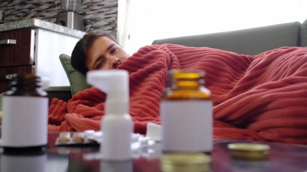 Ingwer, Zitrone, Zwiebeln und verschiedene Medikamente liegen auf dem Tisch des kranken Mannes. Alternativmittel und traditionelle Pillen gegen Erkältungen und Grippe. Kranker Mann in rote Decke gehüllt - Filmmaterial, Video