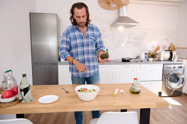 Knappe mannelijke chef-kok gekleed in casual kleding, koken van een gezonde salade in de minimalistische huiskeuken. Eten. Mensen. Lifestyle. Gezond eten en dieet concept. - Foto, afbeelding