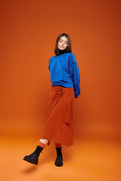 tenue de saison d'automne, femme attrayante en jupe et sweat-shirt bleu debout sur fond orange - Photo, image