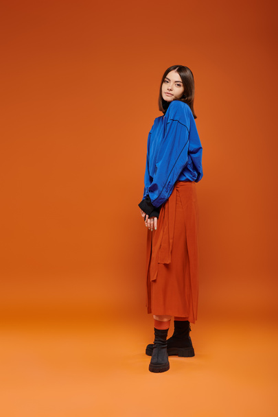 jesienna moda, piękna kobieta w spódnicy, niebieska bluza i buty stojące na pomarańczowym tle - Zdjęcie, obraz