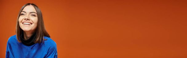 банер, щаслива жінка з проколотим носом дивиться в сторону і посміхається на помаранчевому тлі, синій светр - Фото, зображення