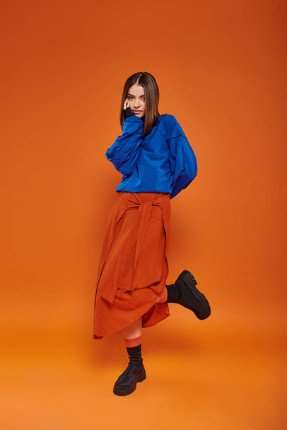 fashionable and young woman with pierced nose standing in autumn skirt and boots on orange backdrop - Photo, Image