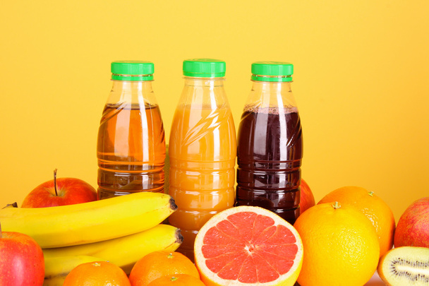 Bottles of juice with ripe fruits on yellow background - Foto, Imagen