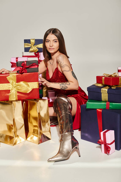 привлекательная женщина в стильном праздничном платье и туфли позируют возле подарков, концепция праздничных подарков - Фото, изображение