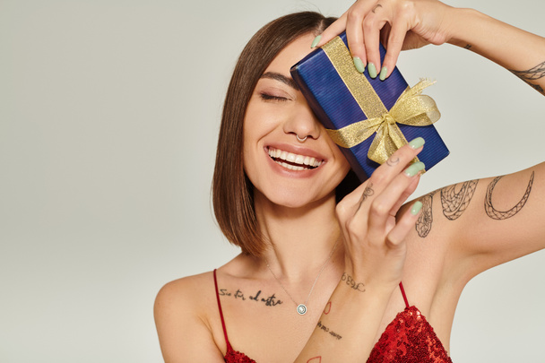 atraktivní dáma se srdečně usmívá se zavřenýma očima s dárečkem před obličejem, vánoční dárky - Fotografie, Obrázek