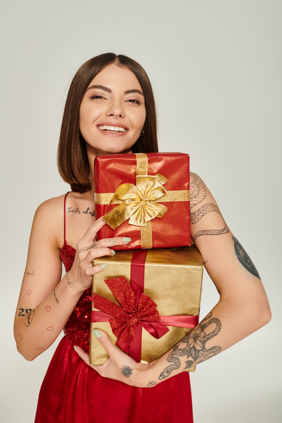 atractiva mujer alegre sosteniendo pila de regalos y sonriendo a la cámara, concepto de regalos de vacaciones - Foto, imagen