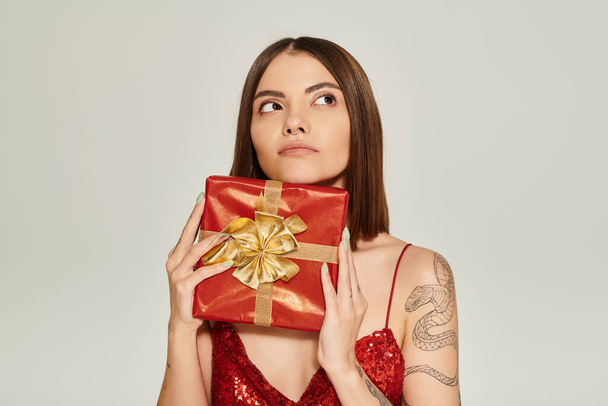 Nachdenkliche junge Frau hält rotes Geschenk in der Hand und schaut träumerisch weg, Konzept für Weihnachtsgeschenke - Foto, Bild
