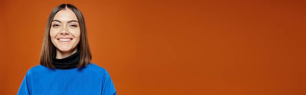 belle femme avec nez percé dans une veste bleue décontractée souriant à la caméra sur fond orange, bannière - Photo, image
