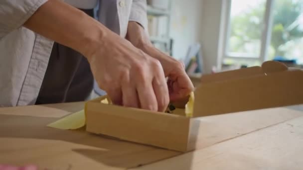 Gesneden shot van vrouwelijke werknemer verpakking edelsteen ketting in kartonnen pakket doos met tissuepapier tijdens de voorbereiding van bestelling voor verzending in online winkel magazijn - Video