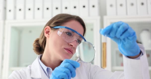Wetenschapper kijkt naar reageerbuis met oplossing door vergrootglas. Onderzoek en ontwikkeling - Video
