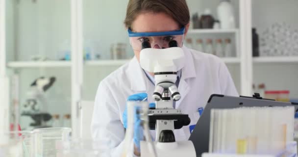 Εγκληματολογικό μικροσκόπιο και γυναίκες που γράφουν σημειώσεις για πληροφορίες σχετικά με πειράματα ή έρευνες στο εργαστήριο. Γυναίκες που συμμετέχουν στη μικροβιολογία και ευκαιρίες για ανακαλύψεις θεραπείας και τεκμηρίωση της - Πλάνα, βίντεο