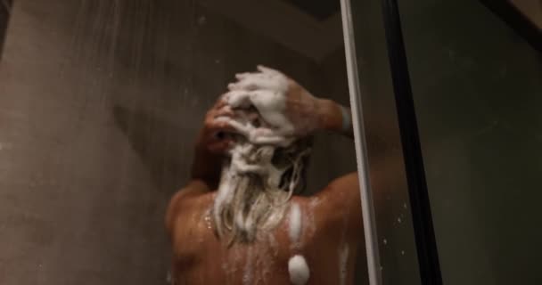 Vue arrière d'une femme lavant les cheveux avec un shampooing et massant la tête recouverte de mousse debout sous l'eau qui tombe. Soins capillaires cosmétiques - Séquence, vidéo