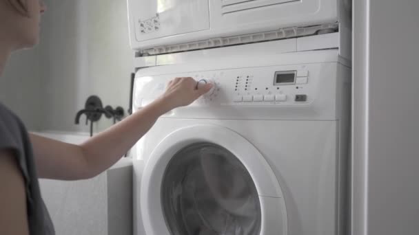 Жінка вмикає пральну машинку, вибирає цикл для прання одягу і починає прати - Кадри, відео
