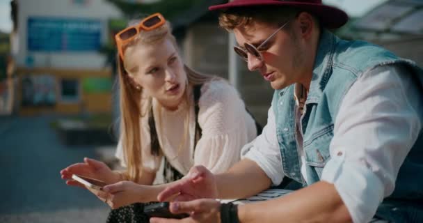 Szőke fiatal nő beszél férfi barátja használja a mobiltelefon a napsütéses napon - Felvétel, videó