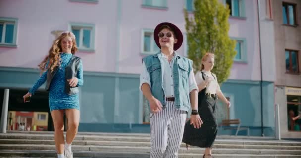 Junge Freundinnen und Freunde in trendigen Outfits laufen gegen Gebäude in der Stadt - Filmmaterial, Video