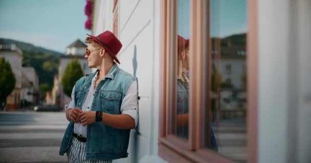 Στοχαστικός νεαρός κοιτάζει γύρω ενώ γέρνει στο κτίριο στο μονοπάτι - Πλάνα, βίντεο