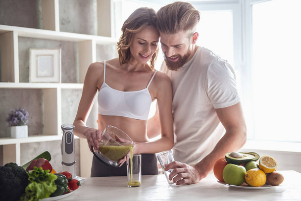 Bella giovane coppia sta parlando e sorridendo mentre cucina cibo sano in cucina a casa - Foto, immagini