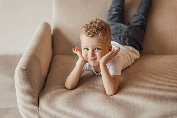 Pieni vaalea poika keltaisessa nojatuolissa katsoo pois hymyillen. Tekstiavaruus. Kansainvälinen lasten päivä - Valokuva, kuva