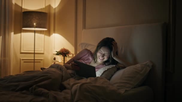 Fille regardant drôle de film vidéo tablette la nuit. Femme heureuse se reposant lit à la maison profitant de contenu en ligne plate-forme de streaming avant de dormir. Jeune femme insouciante utilisant un ordinateur numérique en soirée. - Séquence, vidéo