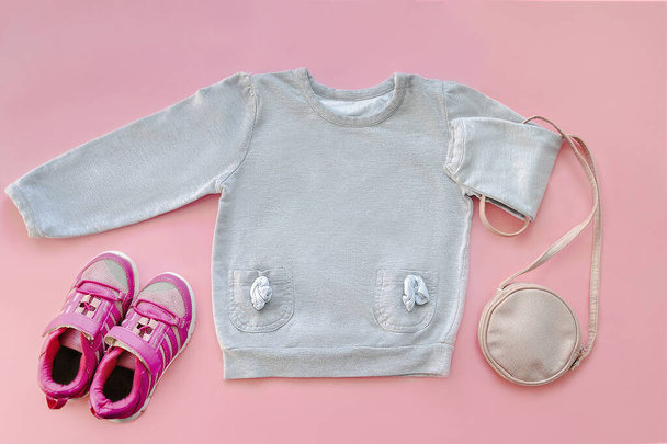 暖かいグレージャンパー、セーター、スニーカー、財布、小さなバッグ。赤ちゃんの子供服のセット、春、秋、ピンクの背景に冬。. - 写真・画像