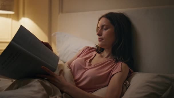 Usmívající se dívka čtení knihy v posteli večer detailní. Uvolněná žena odpočívající před spaním si užívá román v útulném domově. Klidná, klidná studentka, obrací stránku a studuje pozdě v noci. Harmony hobby concept. - Záběry, video