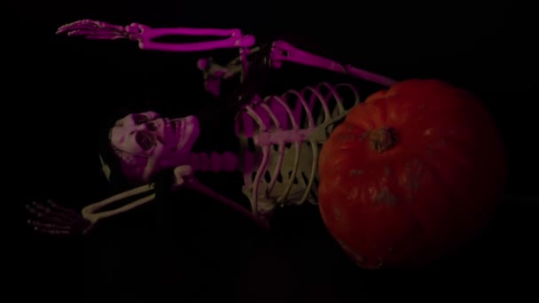 Vista de perto do esqueleto rosa iluminado deitado no fundo preto ao lado da abóbora. Conceito de Halloween. Suécia. - Filmagem, Vídeo