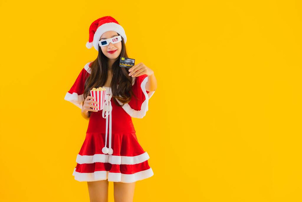 Portré gyönyörű fiatal ázsiai nő visel karácsonyi ruhák kalap popcorn és 3D-s szemüveg kész nézni film sárga elszigetelt háttér - Fotó, kép