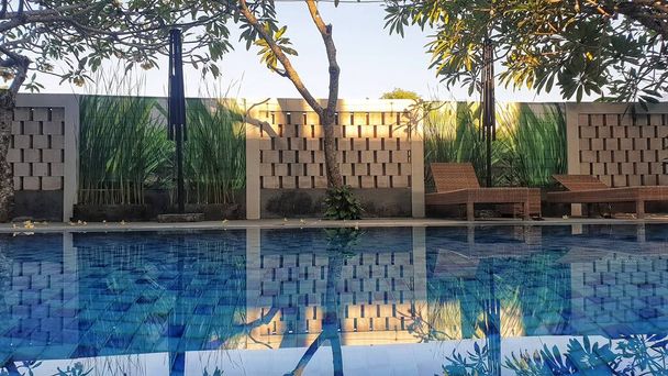Een sereen zwembad omlijst door stoelen en weelderige bomen, biedt een idyllische ontsnapping voor ontspanning en vrije tijd - Foto, afbeelding