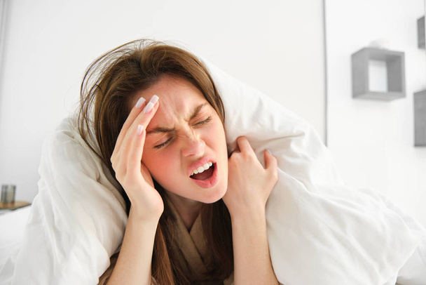 Frau hat morgens Kopfschmerzen, liegt unter Decken im Bett und schreit vor Schmerzen im Kopf. - Foto, Bild