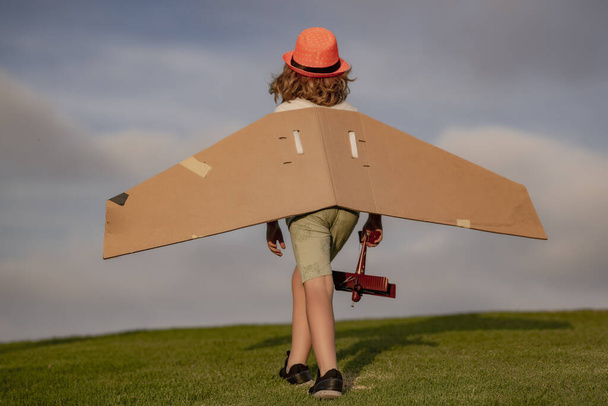 Childhood dream imagination concept. Happy kid playing with toy paper wings outdoors in summer field. Travel and kids vacation concept. Imagination and freedom - Photo, Image