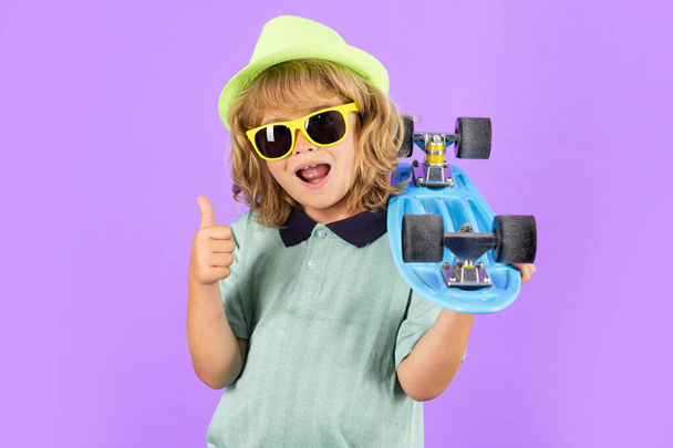 Happy child boy holding skateboard over blue background isolated. Studio portrait of fashion kids - Φωτογραφία, εικόνα