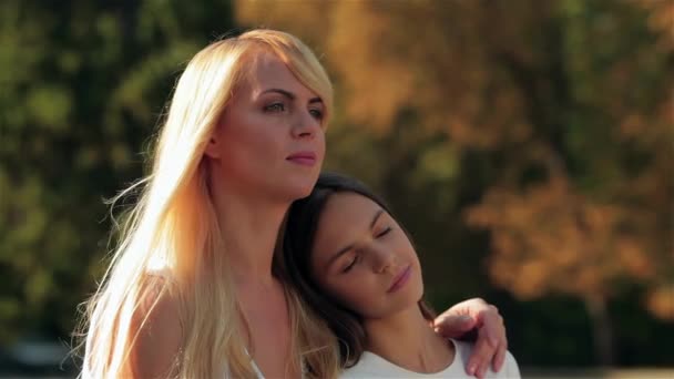 Mother and her teenage daughter are sitting in an embrace on park bench. Happy mother with her daughter in park outdoors. Teenage girl outdoor with her mom. Portrait of mother with teenager daughter - Footage, Video