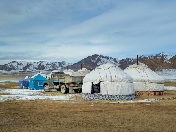 Mongolský jurtový tábor v zimní stepi. Vedle jurt stojí starý náklaďák na pozadí zasněžených hor. - Fotografie, Obrázek