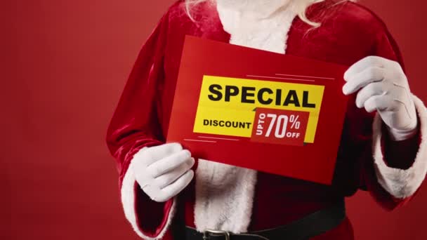 Medium shot of unrecognizable man in traditional Santa Claus outfit holding sign promising special discount for Black Friday sale, on plain red background. Suitable as template, copy space - Footage, Video