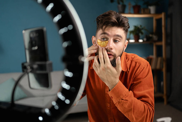 Mužský blogger kosmetolog nahrávání tutorial o použití kosmetiky vede vlog na sociálních sítích, pomocí skvrn pod očima pro péči o pleť. Vliv na prodej kosmetiky na sociální síti - Fotografie, Obrázek