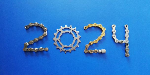 2024 Ciklusok koncepció háttér arany lánc és kerékpár alkatrész kék háttér - Fotó, kép