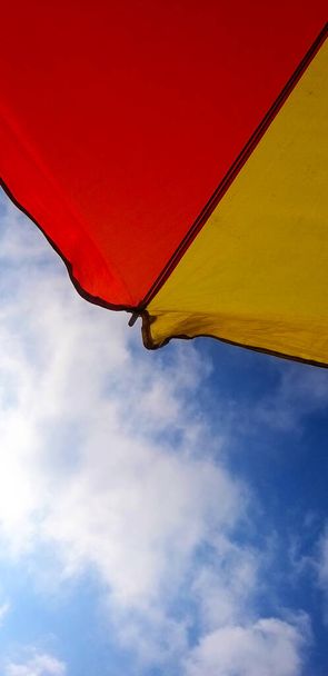 кусочки красного и желтого зонтов на голубом фоне неба - Фото, изображение