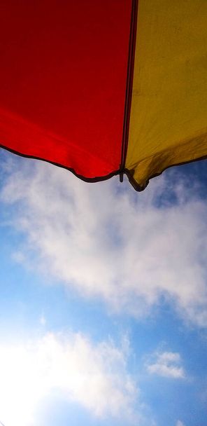 шматочки червоних і жовтих парасольок на фоні блакитного неба - Фото, зображення