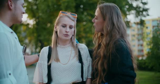 Zamartwiona blondynka rozmawia z przyjaciółmi w ogrodzie o zachodzie słońca - Materiał filmowy, wideo