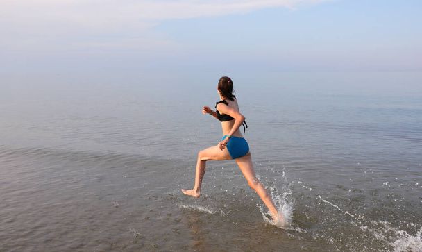 esbelta chica corriendo con muy amplios pasos en la orilla del mar en verano - Foto, Imagen