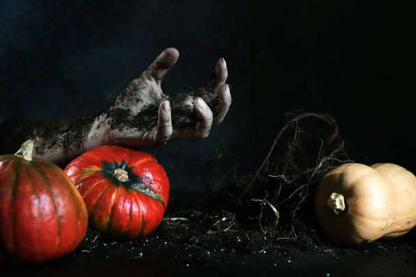 A mão zumbi sai da sepultura. Conceito de evento de férias de Halloween. Mão no chão, raízes de plantas e abóboras. A mão alcança algo - Foto, Imagem