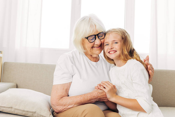 Woman family child granddaughter old generation lifestyle home hug sofa elderly love grandmother girl sitting mother senior couch happy daughter - Photo, Image