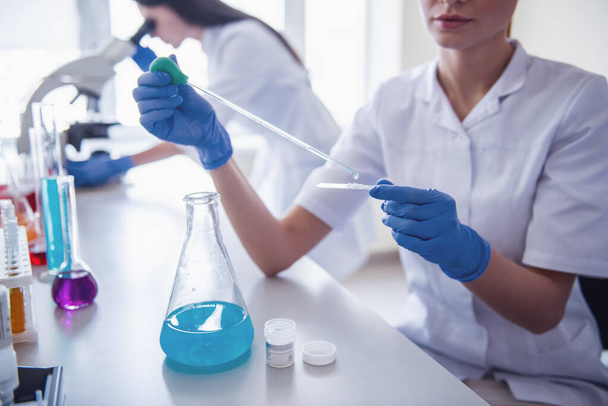 Обрезанное изображение врачей в перчатках, работающих с веществами в пробирках и микроскопе в лаборатории
 - Фото, изображение