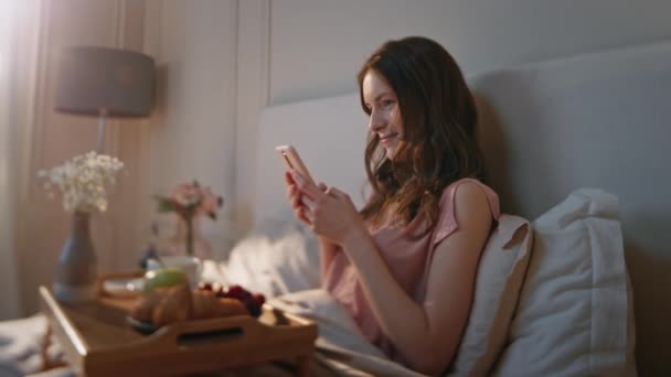 Χαρούμενη γυναίκα πληκτρολογώντας smartphone το πρωί. Γαλήνιο ονειρεμένο κορίτσι απολαύσετε το πρωινό χρόνο ξαπλωμένος στο άνετο κρεβάτι. Ευτυχισμένο ελκυστικό θηλυκό ανάγνωση sms social media στο κινητό τηλέφωνο. Ηρεμία έννοια αναψυχής Σαββατοκύριακο. - Πλάνα, βίντεο