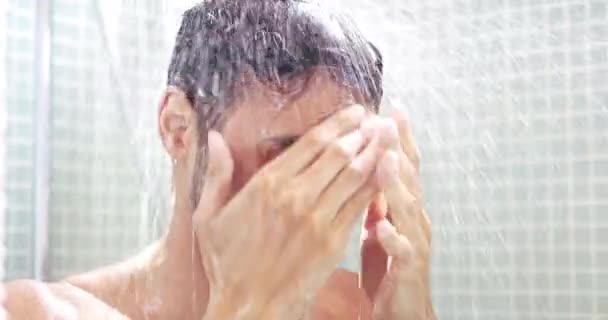 Man, shower and face with water splash in cleaning, washing or hygiene for grooming in bathroom at home. Young, handsome or attractive male person in relax for clean body, care or refreshing at house. - Footage, Video