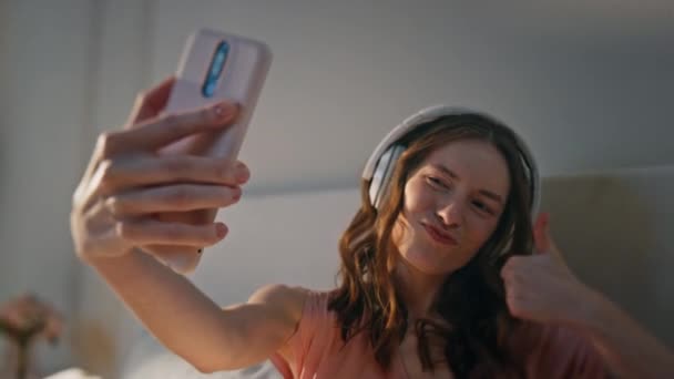 Ευτυχισμένος έφηβος κάνει selfie με ακουστικά closeup. Χαρούμενο κορίτσι που διασκεδάζει βγάζοντας φωτογραφίες smartphone στο σπίτι. Ξέγνοιαστη όμορφη γυναικεία μουσική ακούγοντας απολαμβάνοντας το πρωινό στο σπίτι. Θετικό νέο μοντέλο - Πλάνα, βίντεο